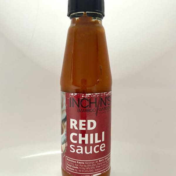 A bottle of Inchin's Bamboo Garden Red Chili Sauce with a red label and black cap.