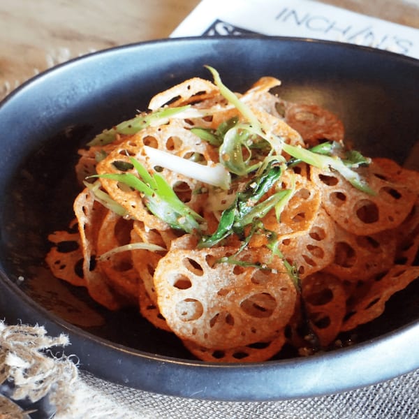 Crispy lotus root chips topped with green onions and sesame seeds in a dark bowl.