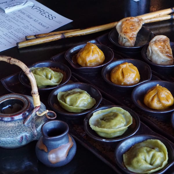 Assortment of colorful Inchin's Bamboo Garden dumplings and potstickers in small dishes with a teapot.