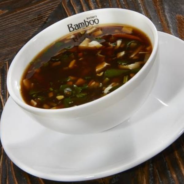 A white bowl of Inchin's Bamboo Garden hot and sour soup with vegetables and mushrooms.