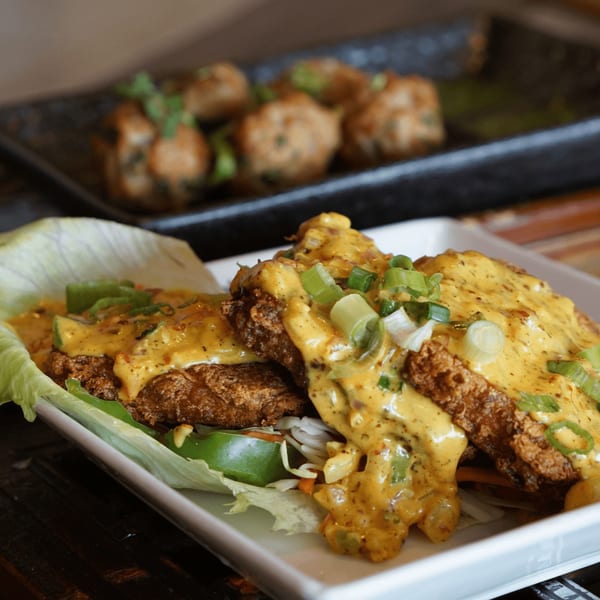 Crispy fried chicken pieces topped with creamy orange sauce and green onions, served with lettuce.