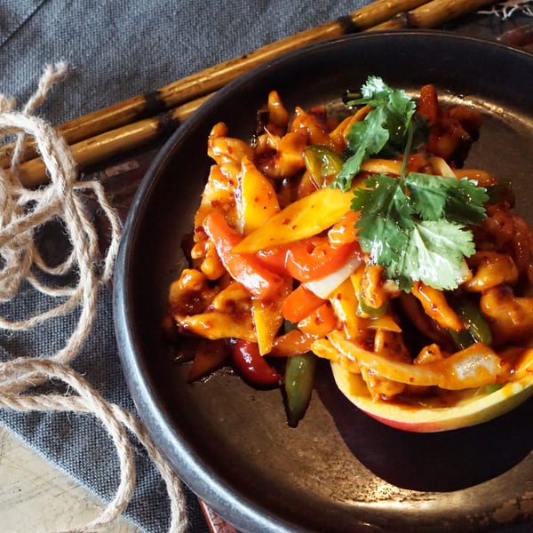 Spicy chicken and bell peppers served in a mango half, garnished with cilantro.