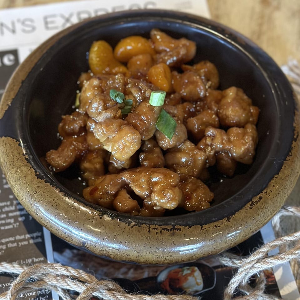Inchin's Bamboo Garden's Asian-fusion dish with glazed chicken and kumquats, garnished with green onions.
