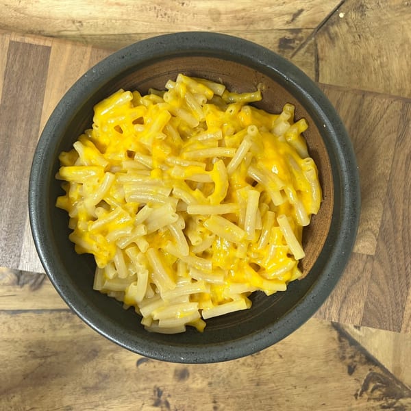 A black bowl filled with macaroni and cheese, featuring elbow pasta coated in bright yellow cheese sauce.