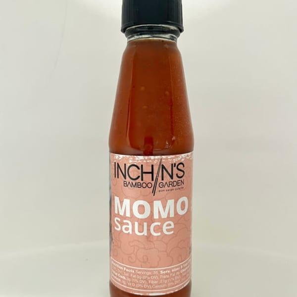 A bottle of Inchin's Bamboo Garden Momo Sauce with a pink label against a white background.