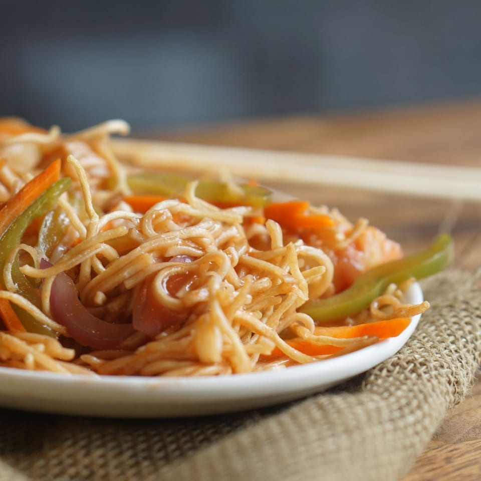 Close-up of Inchin's Bamboo Garden's Asian-fusion noodles with colorful vegetables on a white plate.