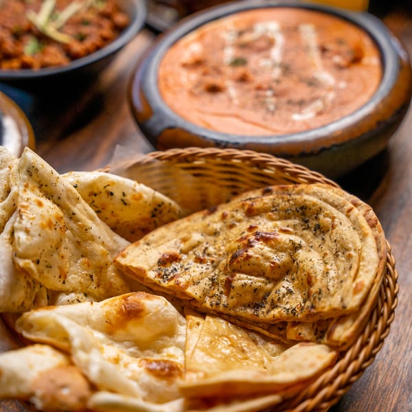A basket of warm naan bread with two bowls of Indian curry in the background.