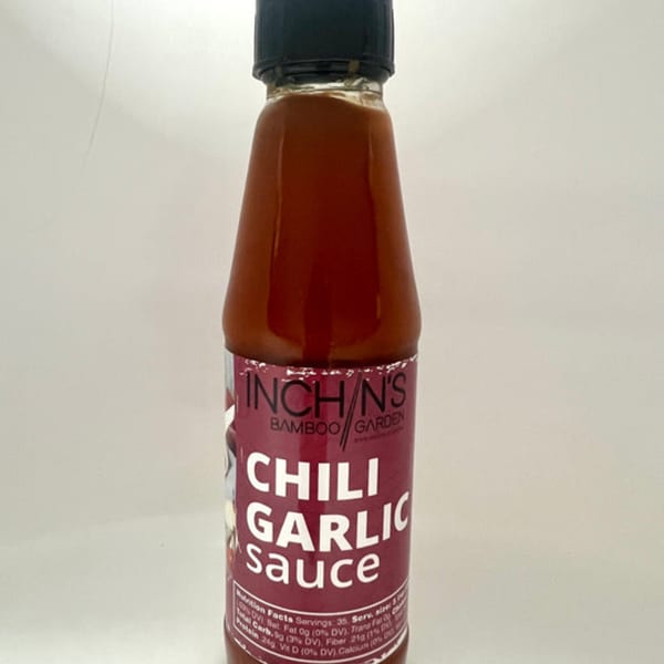 A bottle of Inchin's Bamboo Garden Chili Garlic Sauce with a red label and black cap.