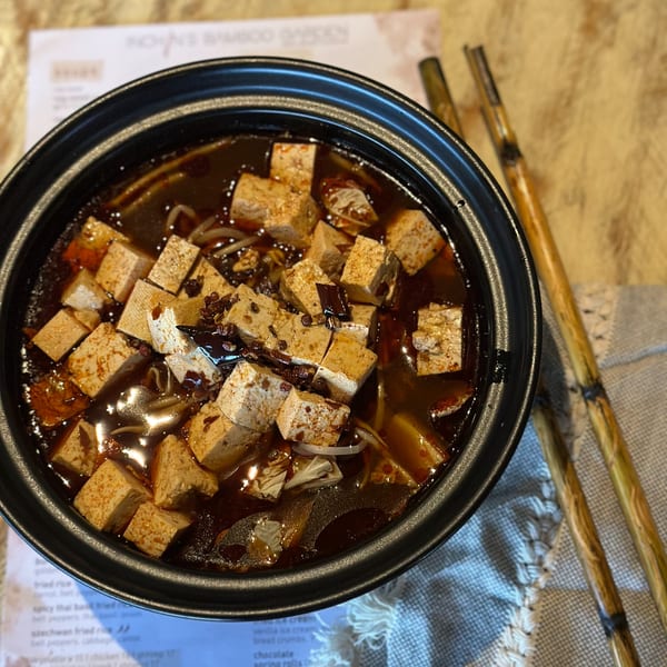 A black bowl of Inchin's Bamboo Garden's spicy Asian-fusion tofu dish with chopsticks on the side.