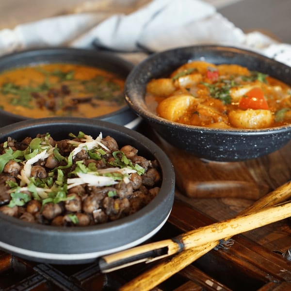 Three bowls of Asian-fusion dishes, including chickpeas and curries, on a wooden tray.