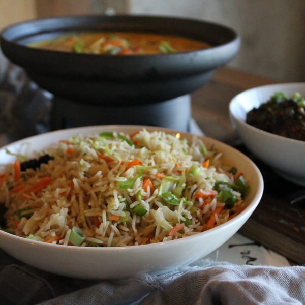 A bowl of vegetable fried rice with carrots, cabbage, and green onions, alongside other Asian-fusion dishes.