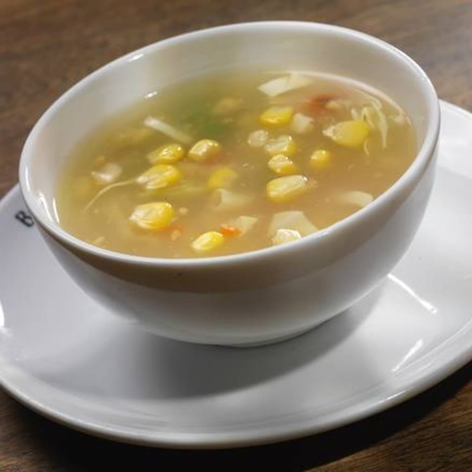 A white bowl of Inchin's Bamboo Garden corn soup with vegetables on a white saucer.