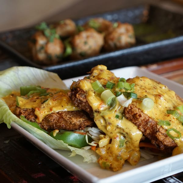 Crispy Asian-fusion chicken with creamy sauce, green onions, and lettuce wraps on a white plate.